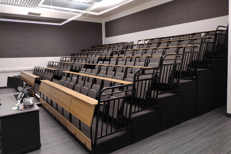A lecture theatre on retractable platforms. There are continuous writing desks in front of each row of chairs.
