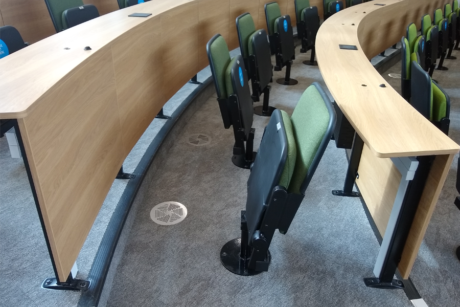 Curved lecture theatre desks. The chairs have swivel bases so that students can work in groups. One of the seats is turned 180 degrees.
