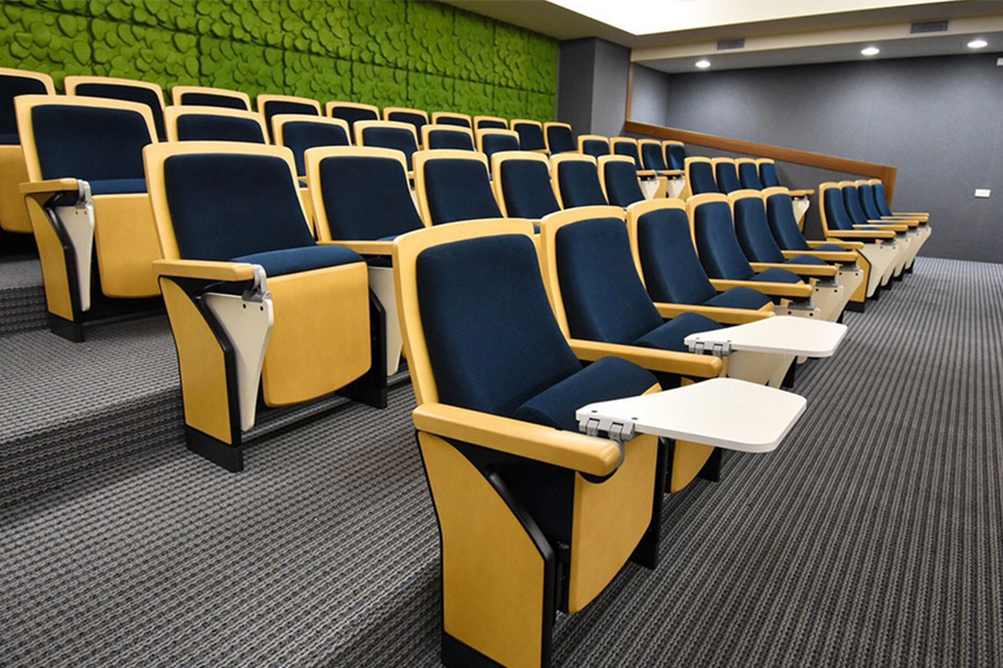 A small contemporary conference room with striking blue auditorium seats, each with a folding writing table.