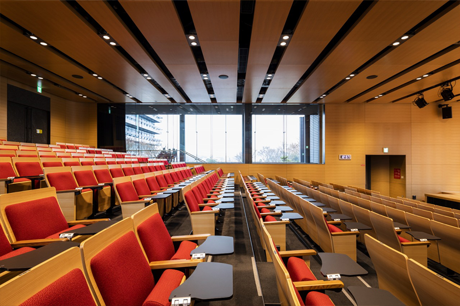 A conference room with high specification seats with timber backs and red upholstery. Folding writing tablets are in place and ready to use.