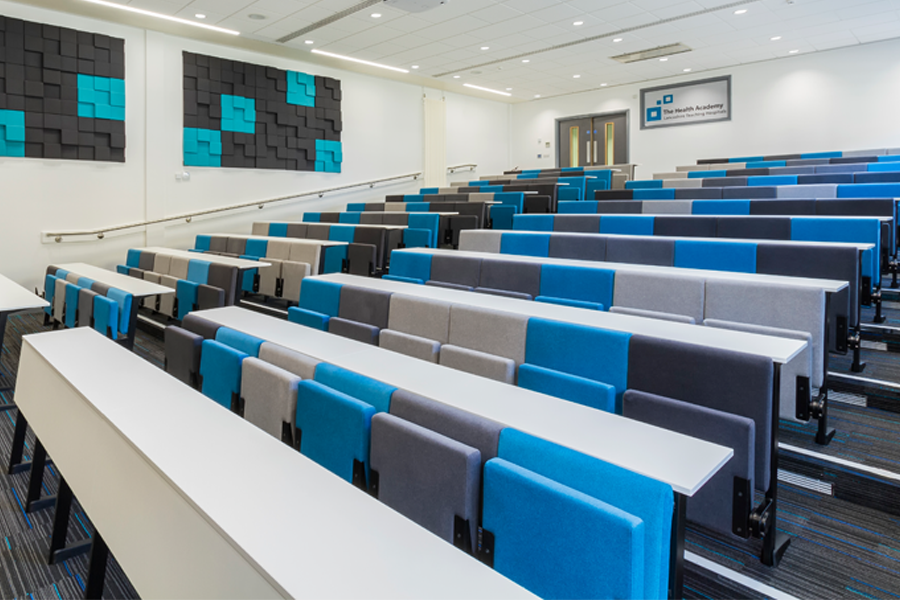 A gently sloping lecture theatre with long white desks and blue and grey seats