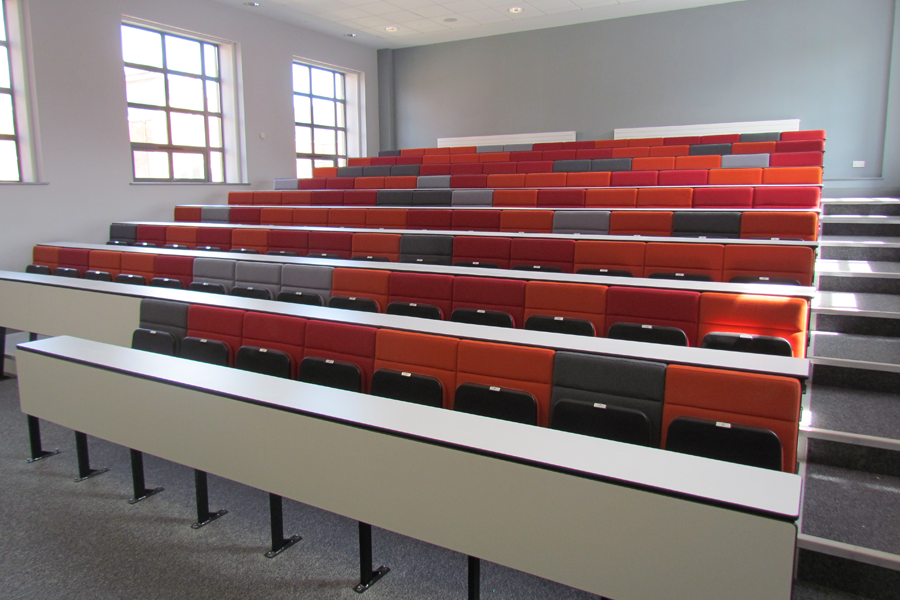 Lecture theatre seating in bright reds and oranges with continuous writing desks.