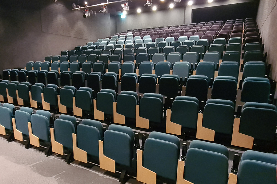 A lecture space with green seats with folding writing tablets.