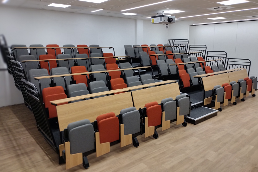 A lecture theatre on retractable platforms. There are continuous writing desks in front of each row of chairs.